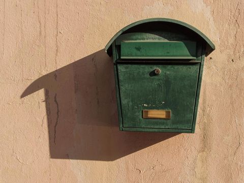 Grüner Metallbriefkasten mit Namensschild an einer sonnigen, verputzten Hauswand