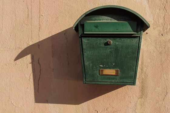 Grüner Metallbriefkasten mit Namensschild an einer sonnigen, verputzten Hauswand
