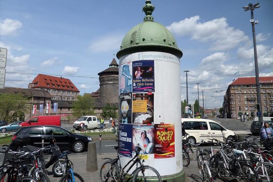 Advertising column covered in concert and theatre posters on a square in Nuremberg, bicycles parked around it