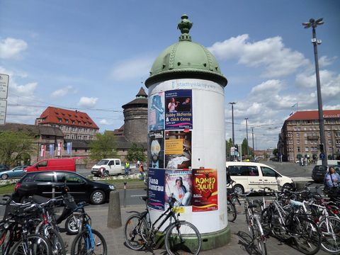 Litfaßsäule mit Konzert- und Theaterplakaten an einem Platz in Nürnberg, davor abgestellte Fahrräder