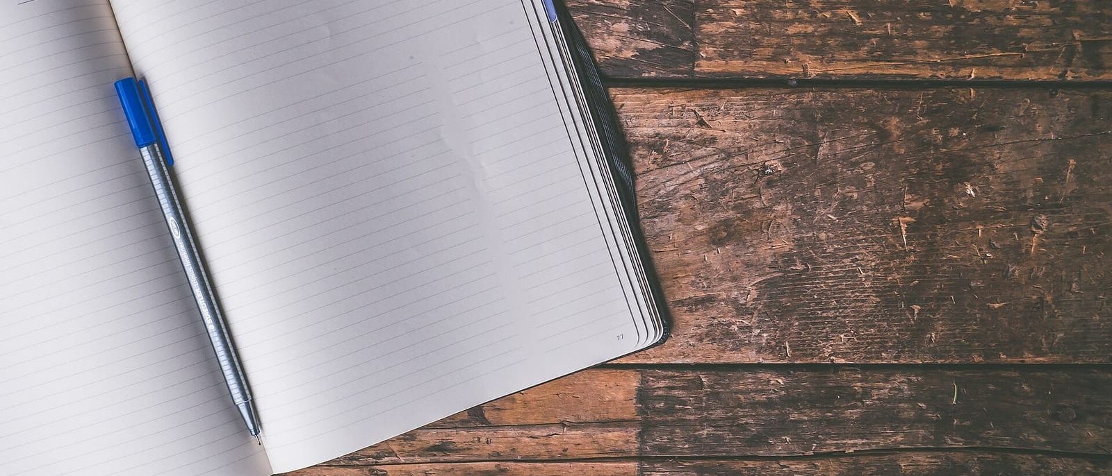 Aufgeschlagenes, leeres Notizbuch mit blauem Stift auf einem alten Holzboden