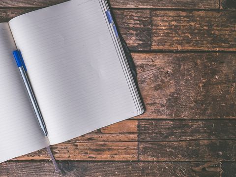 Aufgeschlagenes, leeres Notizbuch mit blauem Stift auf einem alten Holzboden