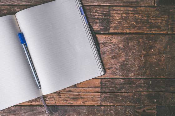 Aufgeschlagenes, leeres Notizbuch mit blauem Stift auf einem alten Holzboden