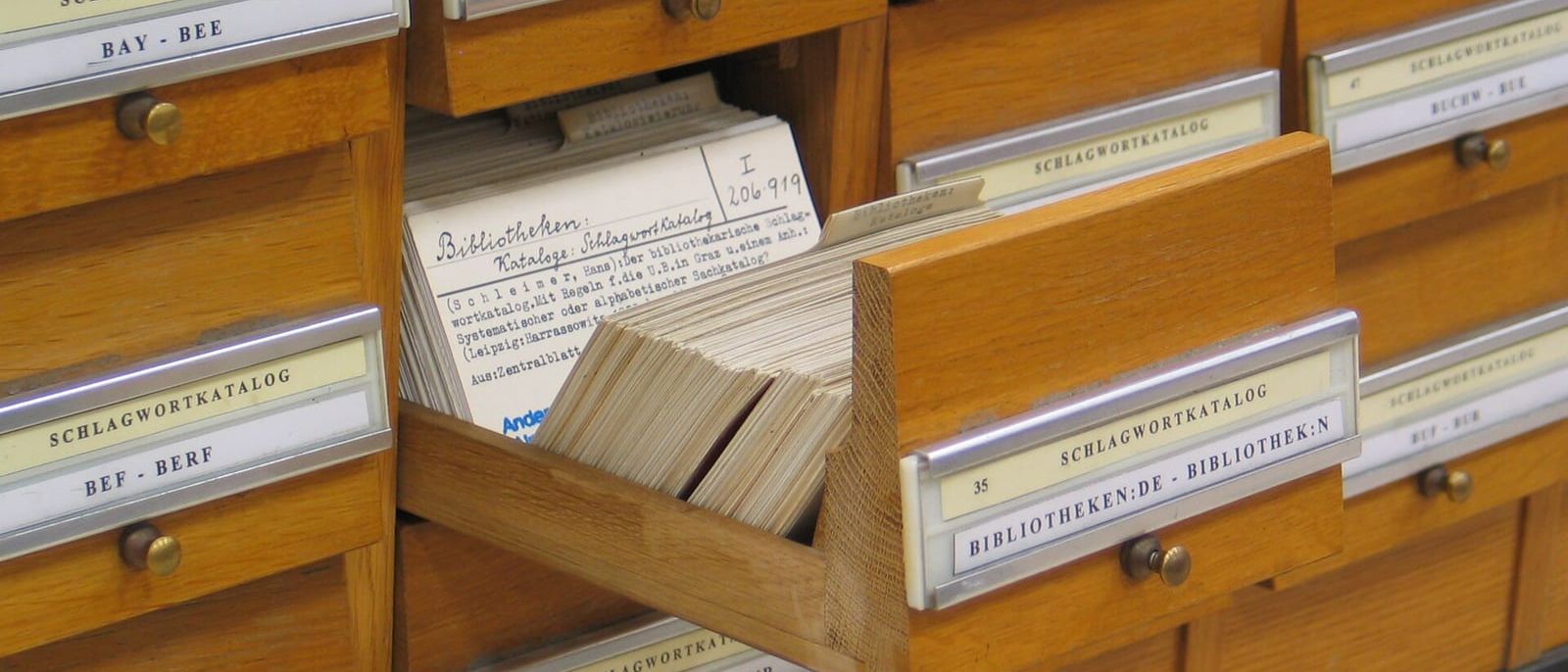 Holzschubladen eines Schlagwortkatalogs in einer Bibliothek, eine Schublade mit Karteikarten ist herausgezogen