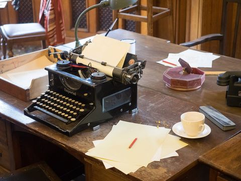 Alte schwarze Schreibmaschine mit eingespanntem Papier auf einem Holzschreibtisch, daneben Teetasse und Notizblätter