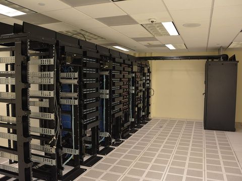 Reihe schwarzer Serverschränke mit blauen Netzwerkkabeln in einem hellen Rechenzentrum