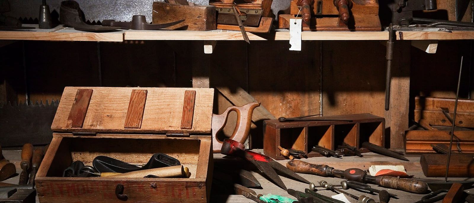 Alte Werkbank mit Hobeln, Sägen, Bohrern und einer offenen Werkzeugkiste aus Holz